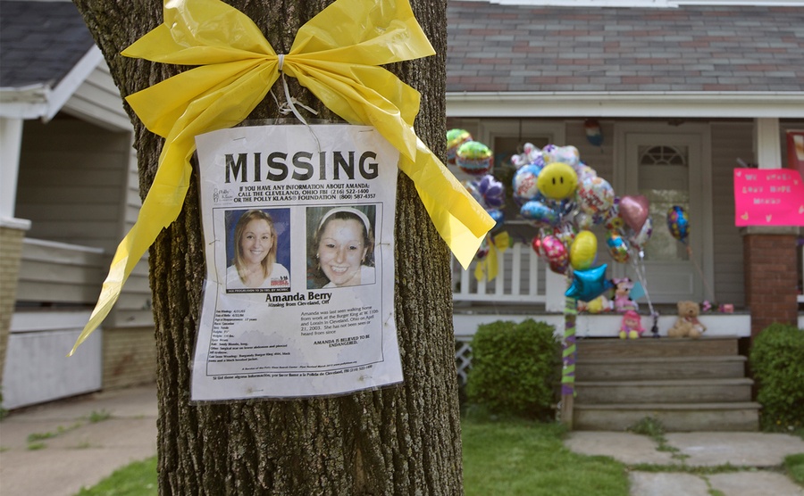 A missing person poster for Amanda Berry hangs on a tree in front of a home. 