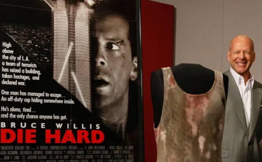 Bruce Willis poses next to the exhibited shirt.