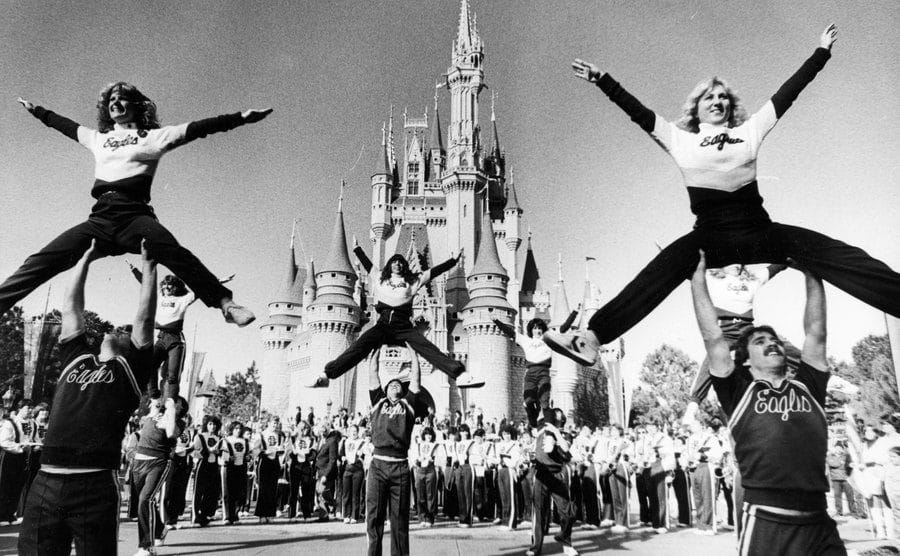 Cheerleaders and a band perform out in front of Cinderella’s Castle.