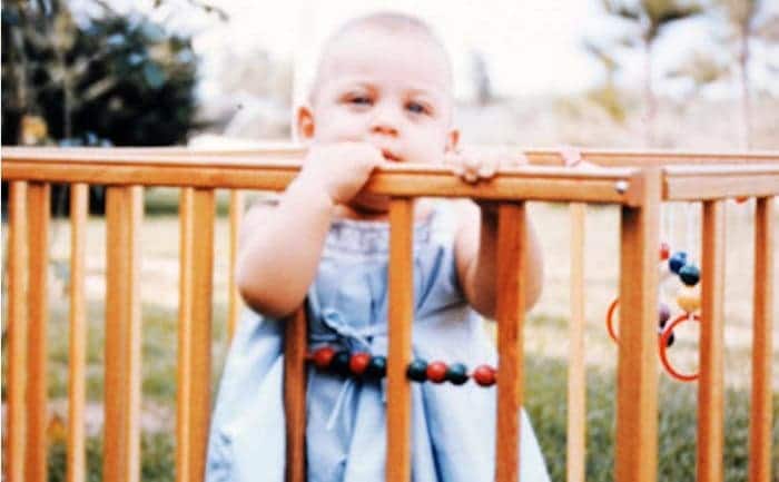 Ellen DeGeneres as a baby in a wooden crib outdoors 