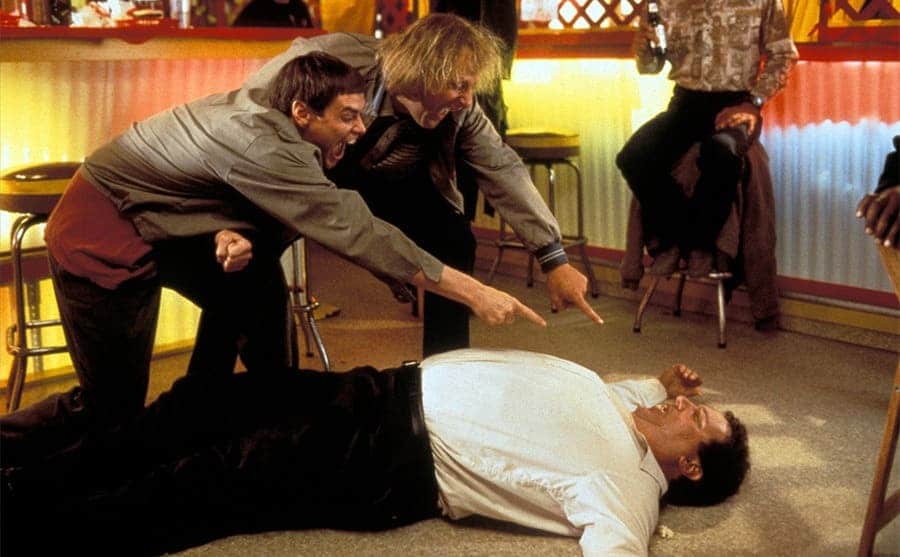 Jim Carrey and Jeff Daniels pointing and laughing at Mike Starr who is lying on the floor in a scene from Dumb and Dumber 