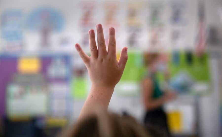A young girl raises her hand in class.