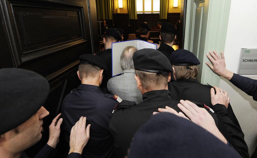 A group of police officers escorts Josef as he enters the courtroom.