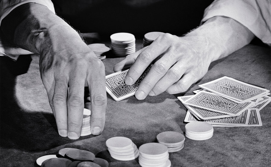 Man hands are playing a game of cards while sitting at a poker table. 