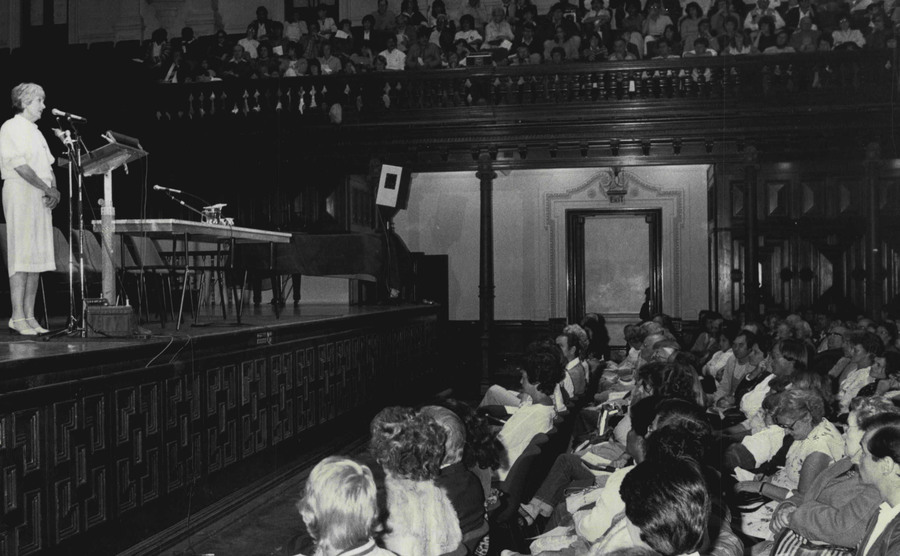 An image of Judy West talking to an almost packed town hall crowd.
