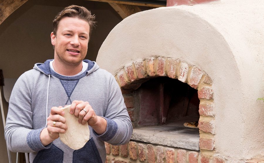 Jamie Oliver cooks a pizza in a stone oven.