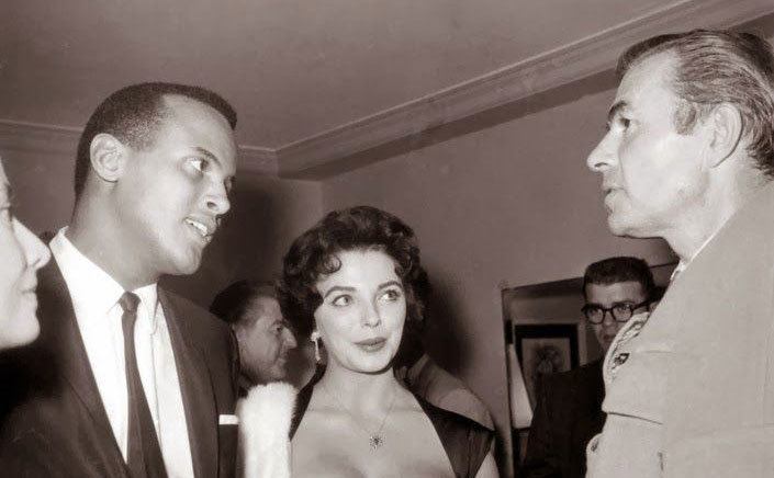Harry Belafonte and Joan Collins talk to guests at a party. 