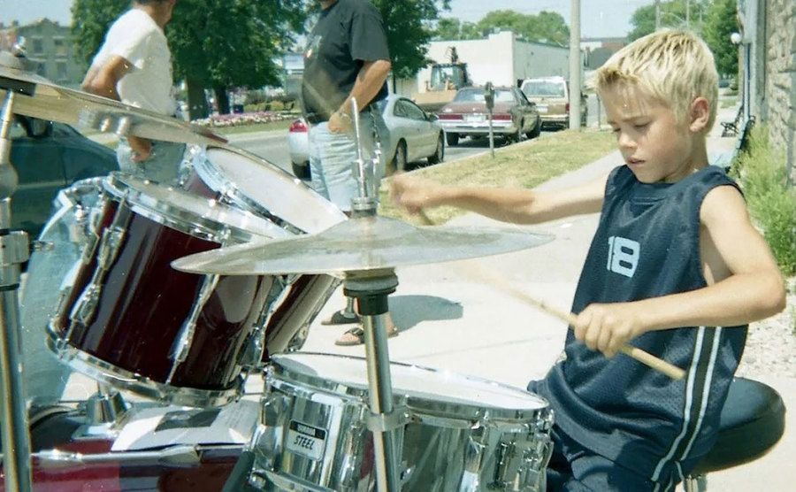 A young Justin Bieber plays the drums on the street. 