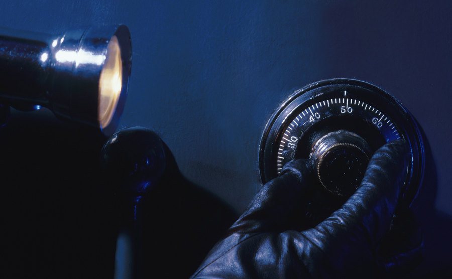 An image of a burglar with a flashlight cracking a safe combination.
