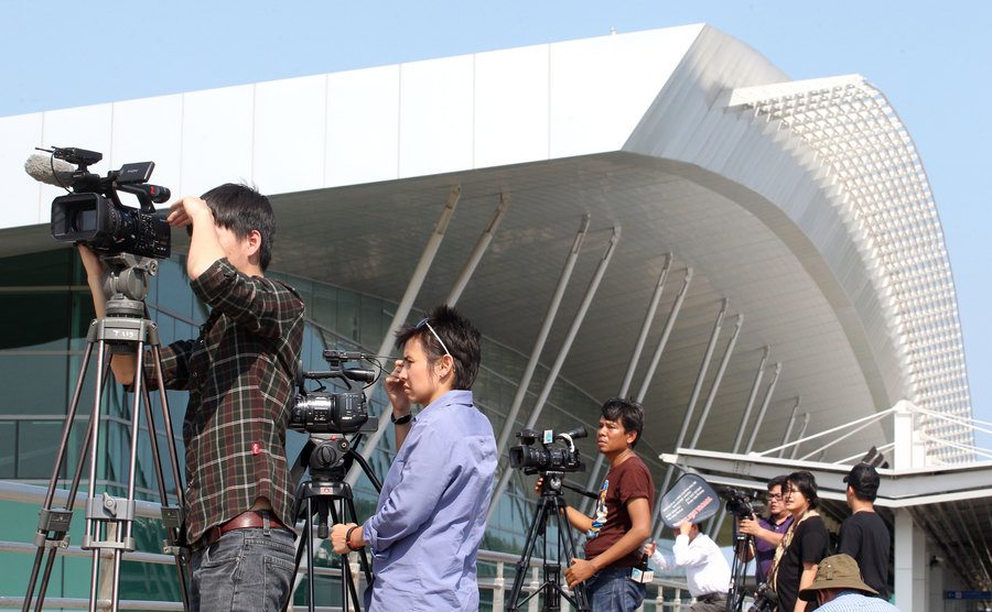Reporters gather outside an airport.