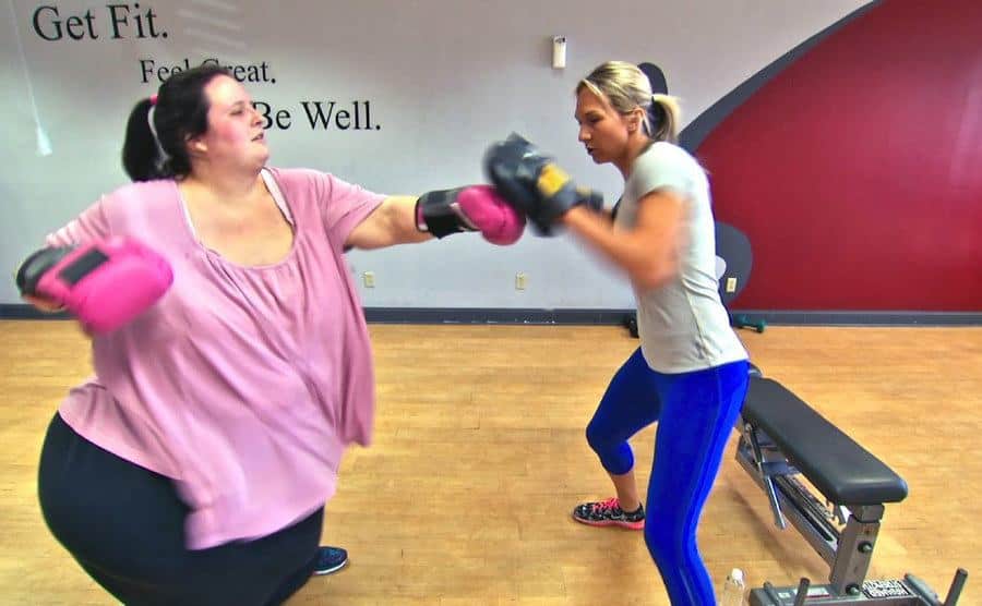 An obese woman is practicing boxing in the gym. 
