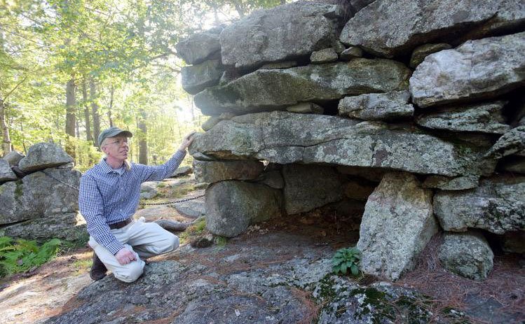 A man crouches beside the entrance to America’s Stonehenge. 