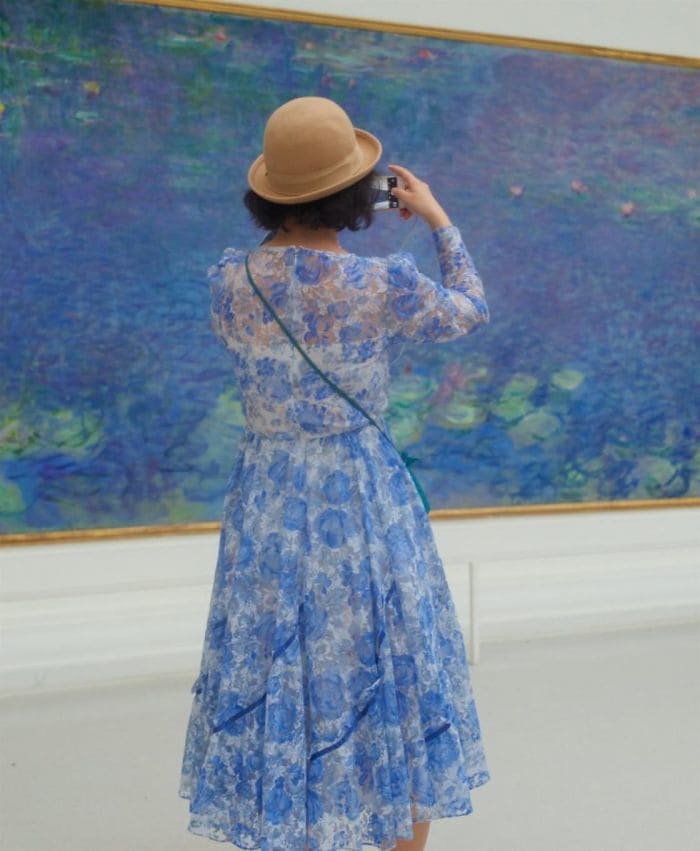 A woman wearing blue flowers photographing a blue and green painting that match.