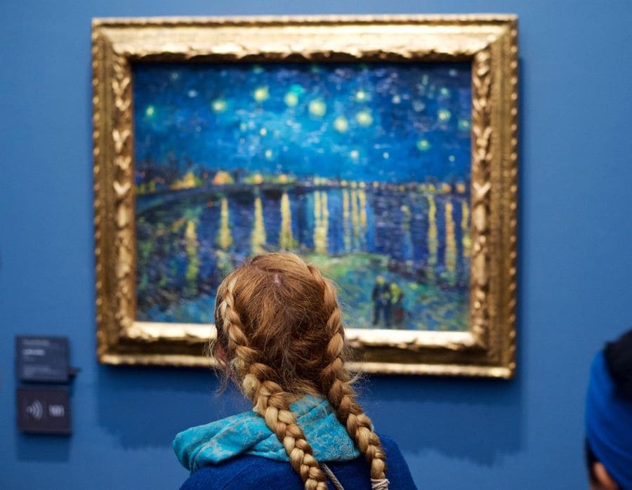 A girl sitting in front of a starry night painting with matching blue clothing and a frame that looks like her braids.
