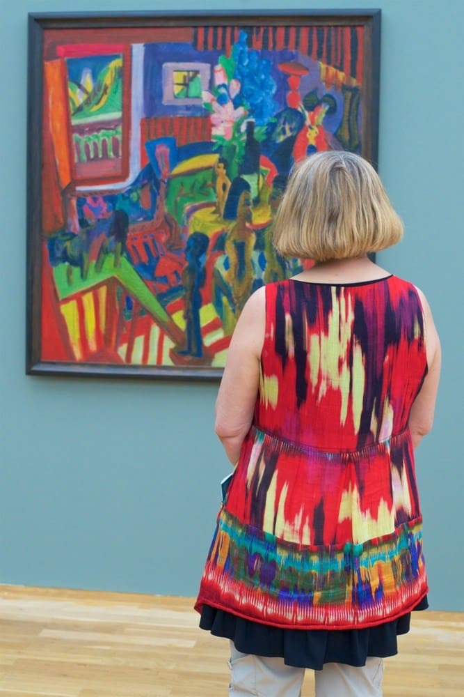 A woman in a colorful dress that matches the colorful painting in front of her.