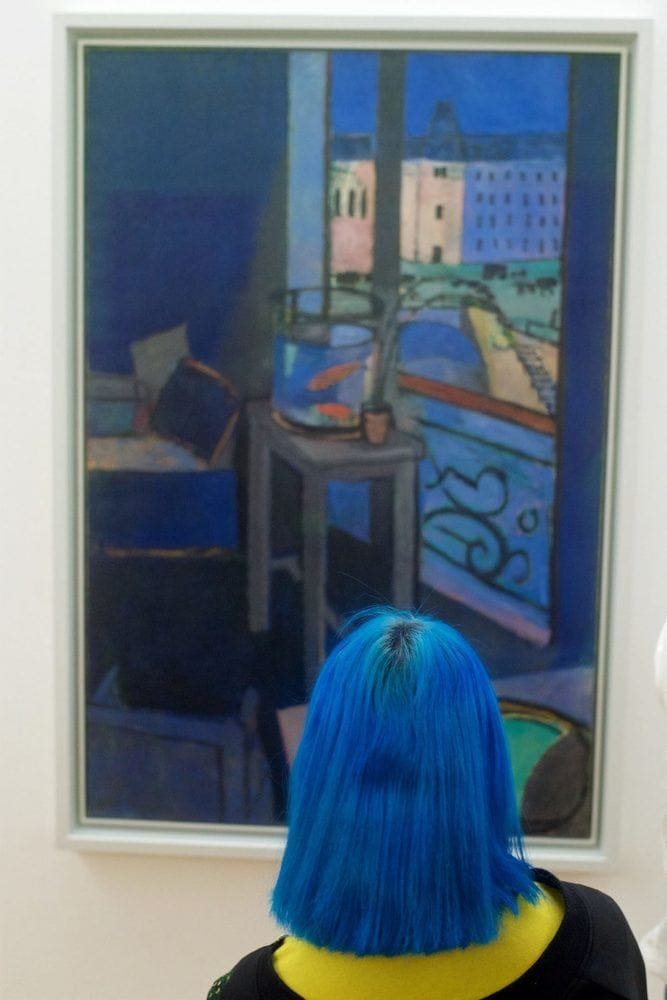 A woman with royal blue hair standing in front of a painting of a royal blue living room.