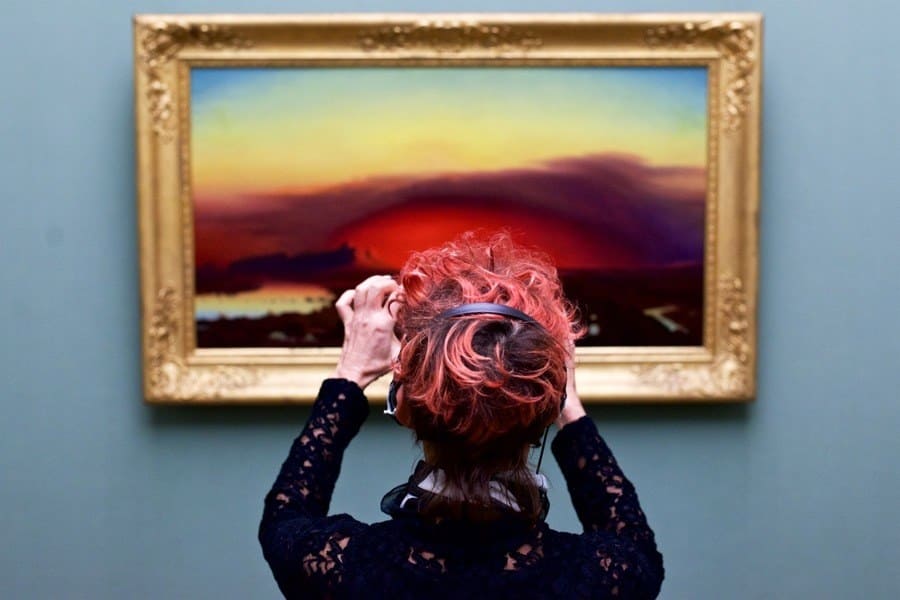 A red-headed woman taking a photo of a beautiful sunset that matches her hair.