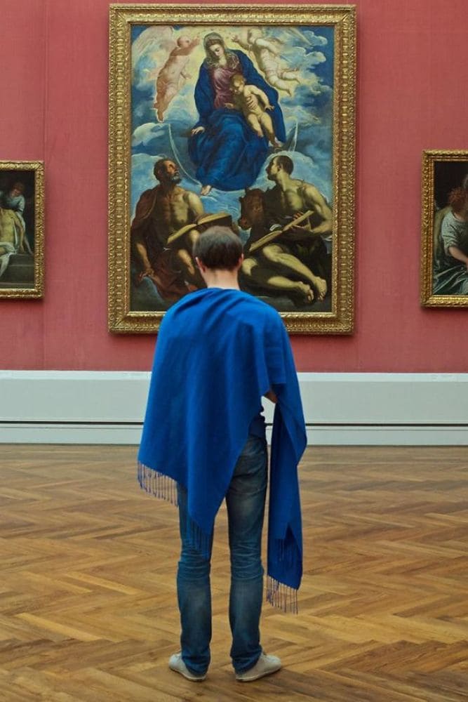 A man with a royal blue shawl draped over him, admiring a painting of someone in a royal blue robe.