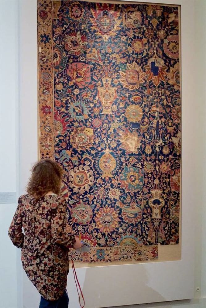 A woman standing in front of an antique navy blue patterned rug wearing a long top which matches the rug.