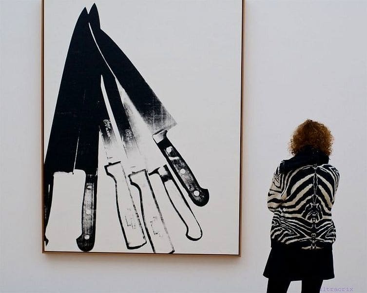A black and white painting of knives which match the striped zebra shirt worn by the woman admiring it.