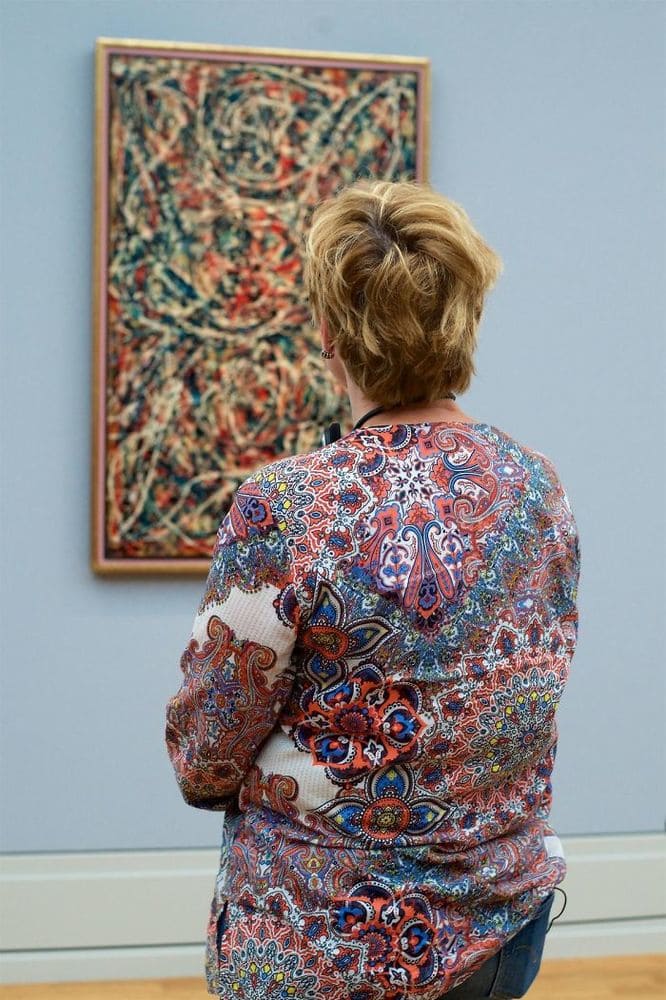Woman with an argyle patterned shirt that matches the slightly blurred painting she is admiring.