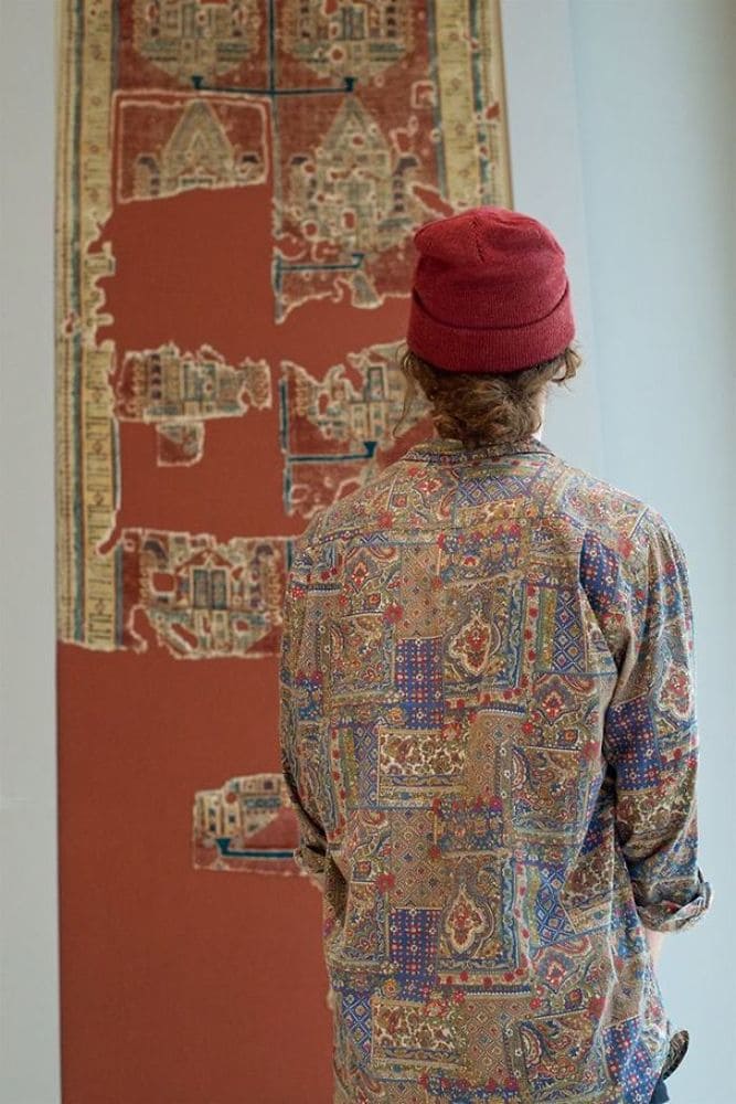 A person with argyle and other random patterned shirt and warm red hat, which matches the artwork’s patterns.