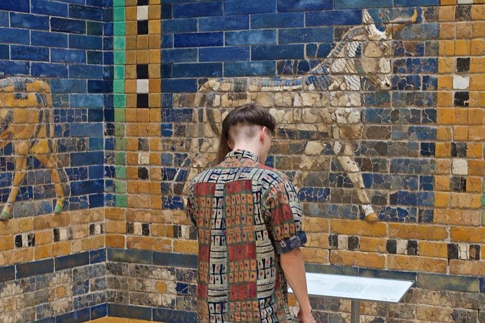 A blue and yellow tiled wall with an animal that is similar looking to the man’s shirt who is standing and reading about it.